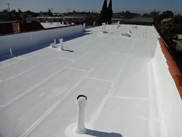 A flat white roof with multiple vents and pipes, under a clear CA sky, with neighboring rooftops and trees visible—ideal work for a skilled roofing contractor in Orange & Los Angeles County.