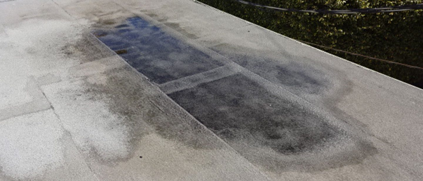 A flat, light gray roof in CA with a large, dark, rectangular wet patch hints at pooling water—an issue best inspected by a roofing contractor serving Orange & Los Angeles County. Smaller wet areas are also visible nearby.