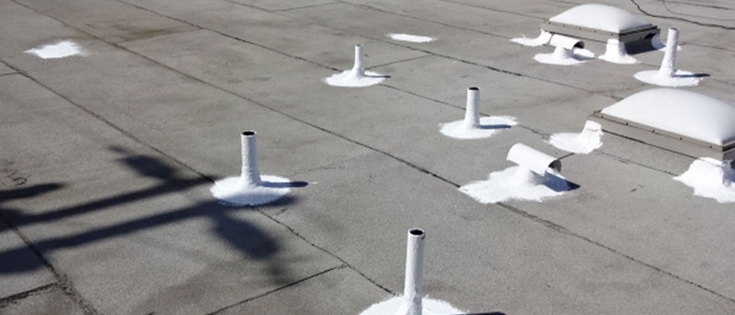 A flat rooftop in CA with multiple white-sealed pipe vents and two domed skylights. Patches of white coating surround each base, contrasting the gray surface—a typical project for a roofing contractor Orange & Los Angeles County.