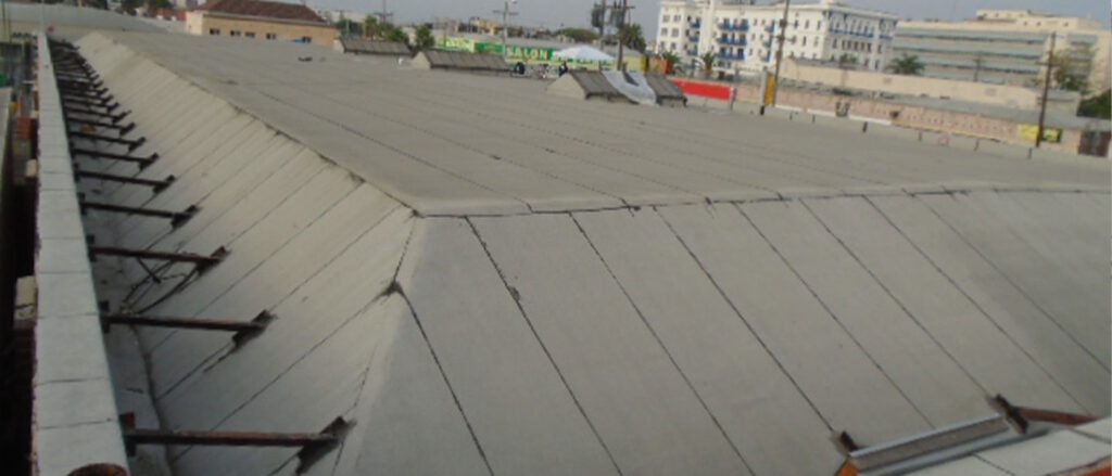 A large, flat, sloped concrete roof structure with support beams on the sides, surrounded by urban buildings and a few trees in the background—ideal for a roofing contractor Orange & Los Angeles County, CA to showcase their expertise.