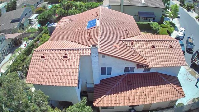 Aerial view of a house with a red tile roof, white chimney, and single solar panel. Located in CA, it’s surrounded by trees, neighboring homes, and a street with parked vehicles—ideal for a roofing contractor Orange & Los Angeles County project.