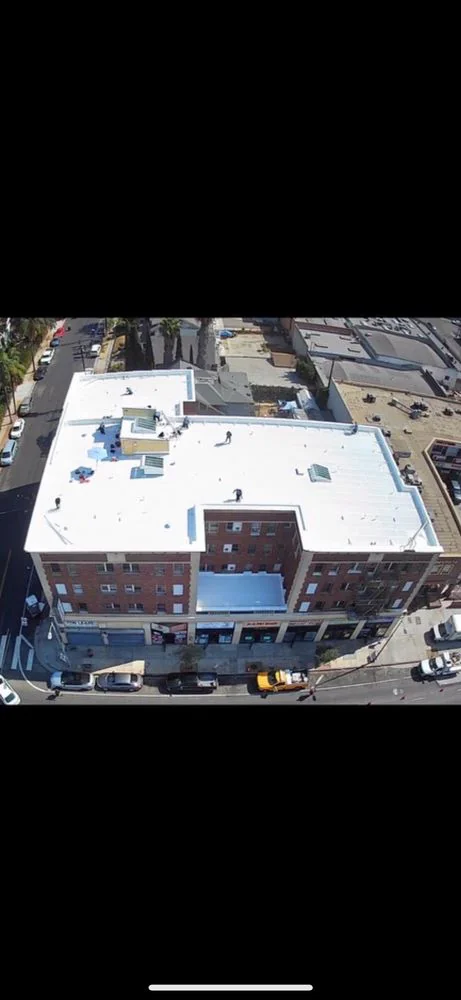 Aerial view of a white commercial roof in Los Angeles County, CA, showing clean lines, reflective coating, and surrounding buildings