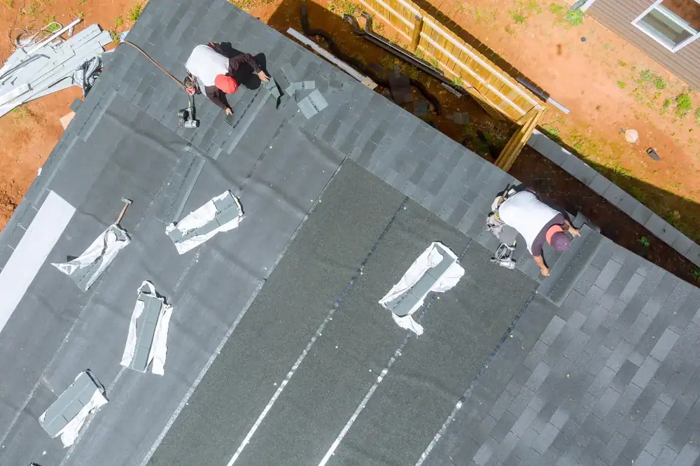 Roofing workers installing asphalt shingles on residential roof.