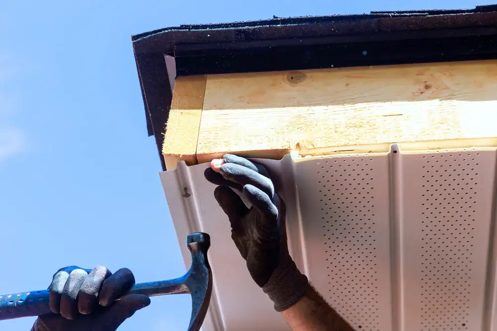 Worker installing vinyl roofing on a house gutter system.