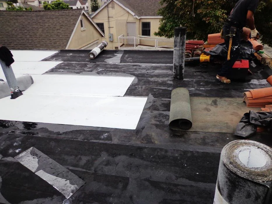 Roofing work in progress on a residential property in Los Angeles County, California, with crew members on the roof