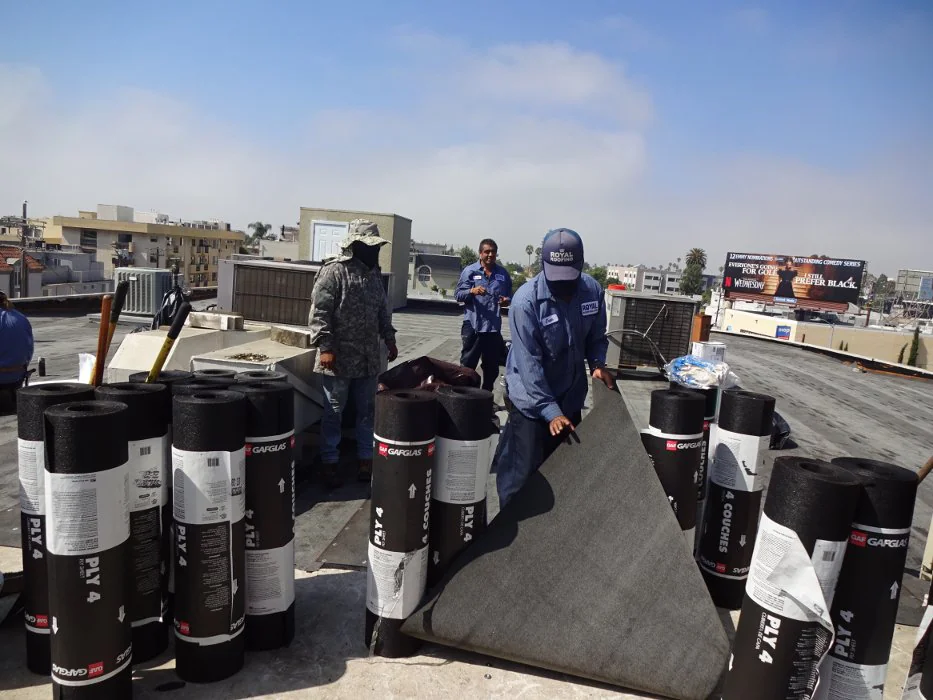 Workers on a rooftop install roofing material on a residential property in Los Angeles County, California, using safety gear and tools during an exterior roofing project