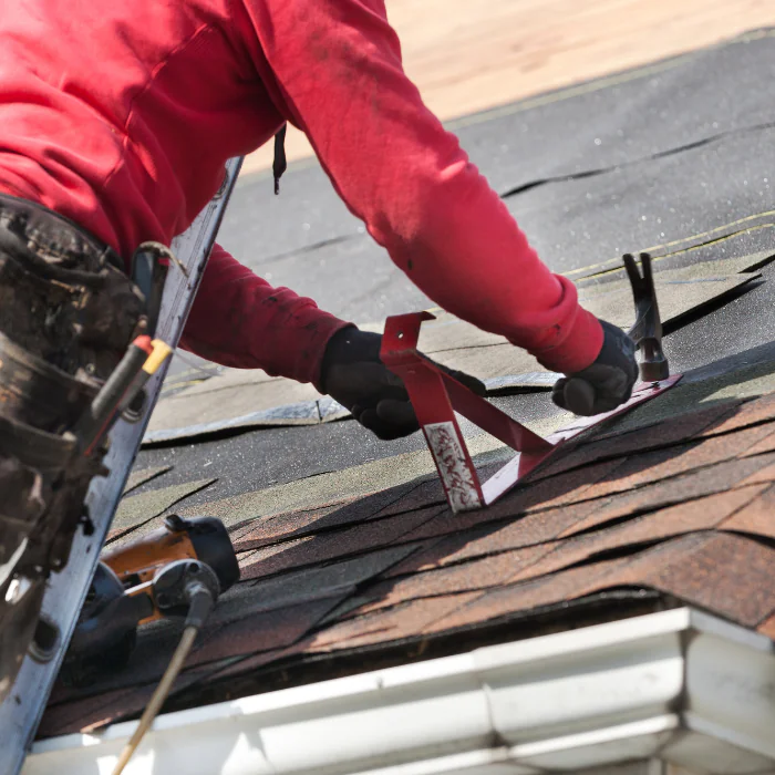 Roofer working on a residential roof in Orange County, California, inspecting shingles and making repairs under clear daytime skies