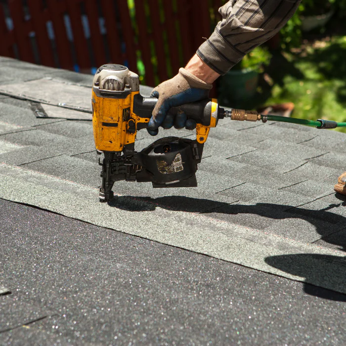 Roofing contractor operating a nail gun while installing shingles on a home roof in Orange County, California